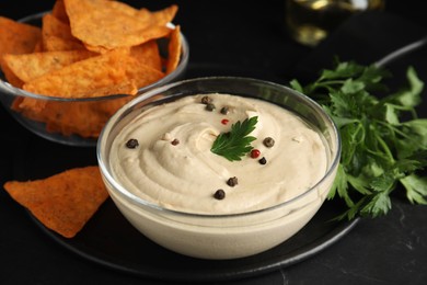 Delicious hummus with nachos and parsley on black table, closeup