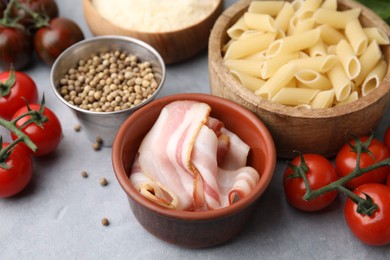 Photo of Raw pasta, bacon and fresh ingredients on light grey table