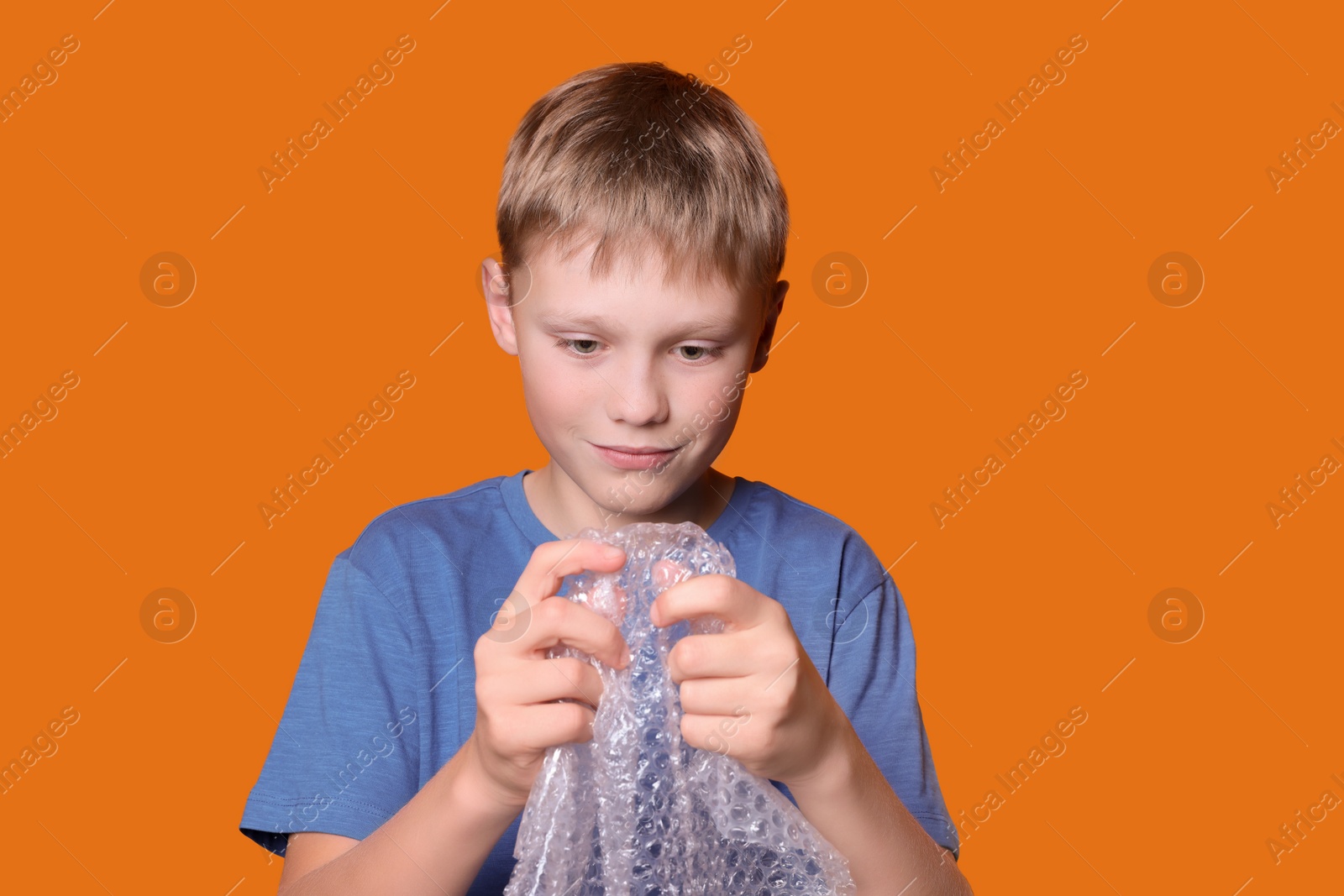 Photo of Boy popping bubble wrap on orange background. Stress relief