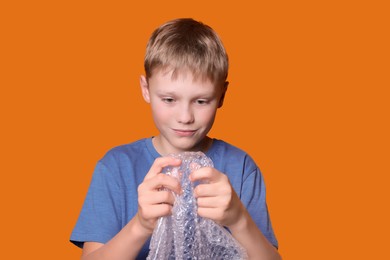 Boy popping bubble wrap on orange background. Stress relief