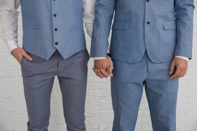 Newlywed gay couple holding hands near white wall, closeup