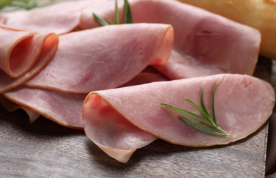 Slices of delicious ham and rosemary on wooden board, closeup