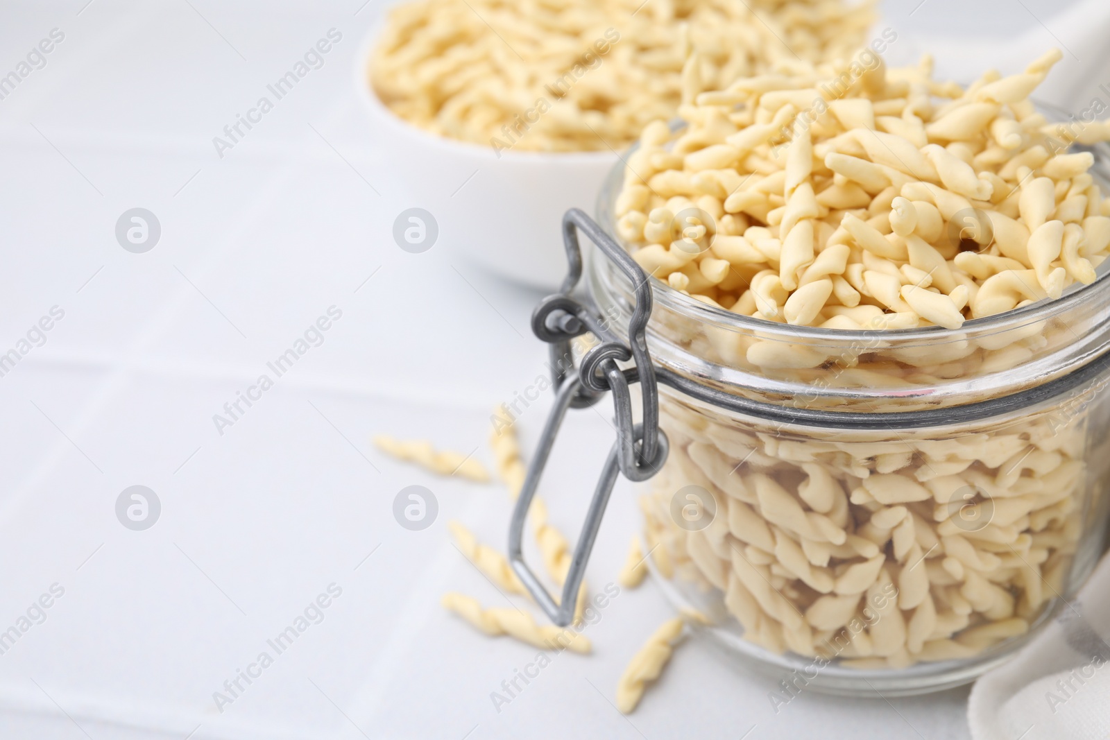 Photo of Uncooked trofie pasta on white tiled table, closeup. Space for text