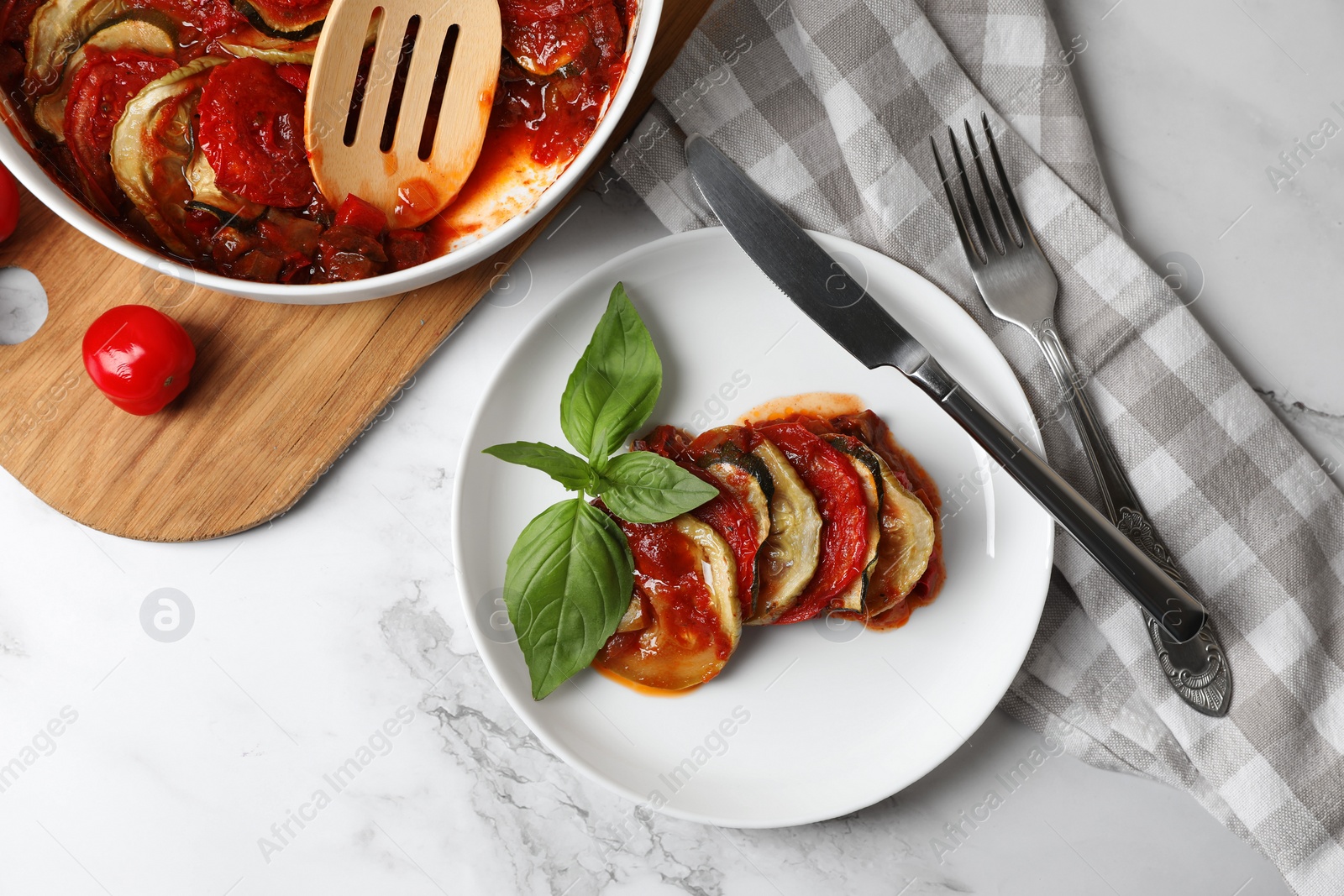 Photo of Delicious ratatouille served with basil on white marble table, flat lay