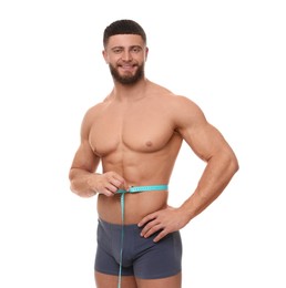 Photo of Portrait of happy athletic man measuring waist with tape on white background. Weight loss concept