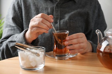 Photo of Woman stirring sugar in tea at wooden table, closeup