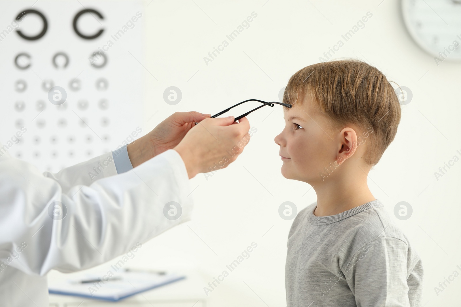 Photo of Vision testing. Ophthalmologist giving glasses to little boy indoors