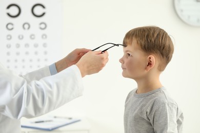 Vision testing. Ophthalmologist giving glasses to little boy indoors