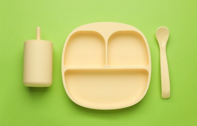 Photo of Set of plastic dishware on light green background, flat lay. Serving baby food
