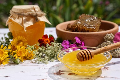 Photo of Delicious honey, combs and different flowers on white wooden table in garden. Space for text