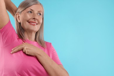 Photo of Beautiful senior woman doing breast self-examination on light blue background, space for text