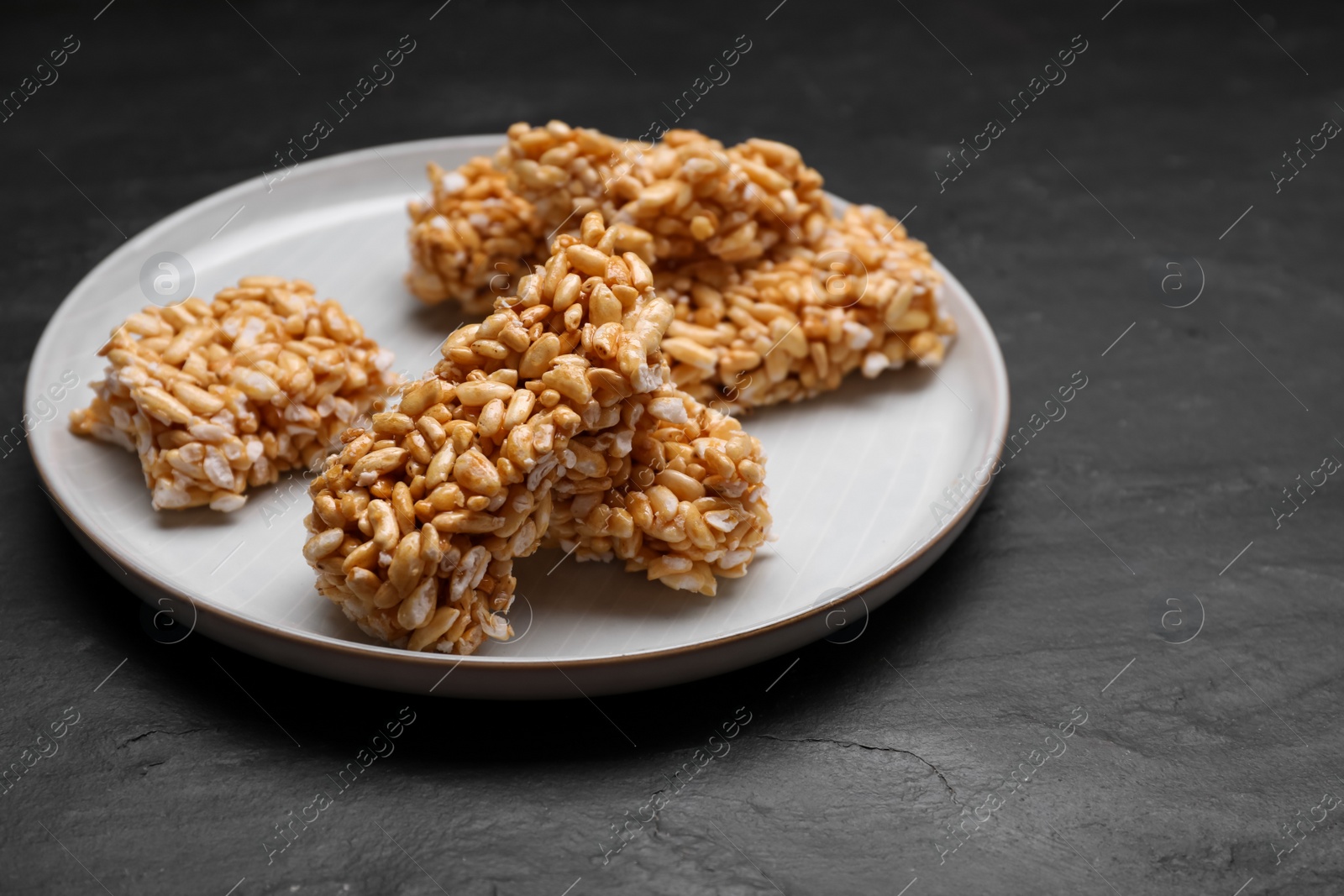 Photo of Plate with puffed rice pieces (kozinaki) on black table, space for text