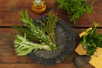 Mortar, different herbs and oil on wooden table, flat lay