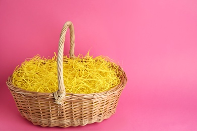 Photo of Easter basket with yellow paper filler on pink background, space for text