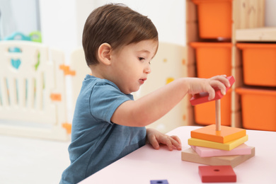 Photo of Little child playing with toy pyramid at table