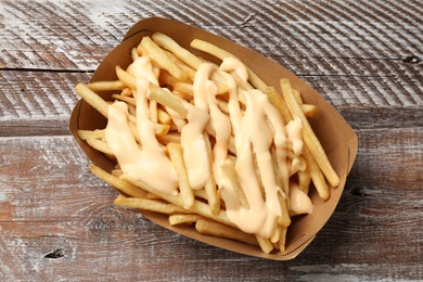 Photo of Delicious French fries with cheese sauce on wooden rustic table, top view