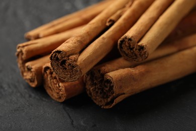 Photo of Dry aromatic cinnamon sticks on black table, closeup