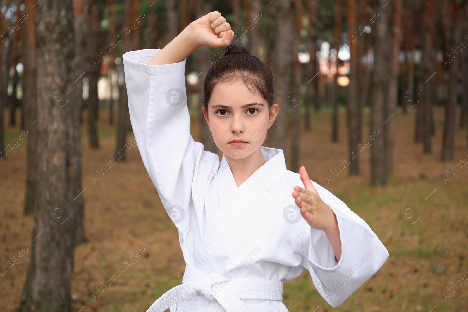 Photo of Cute little girl in kimono practicing karate in forest