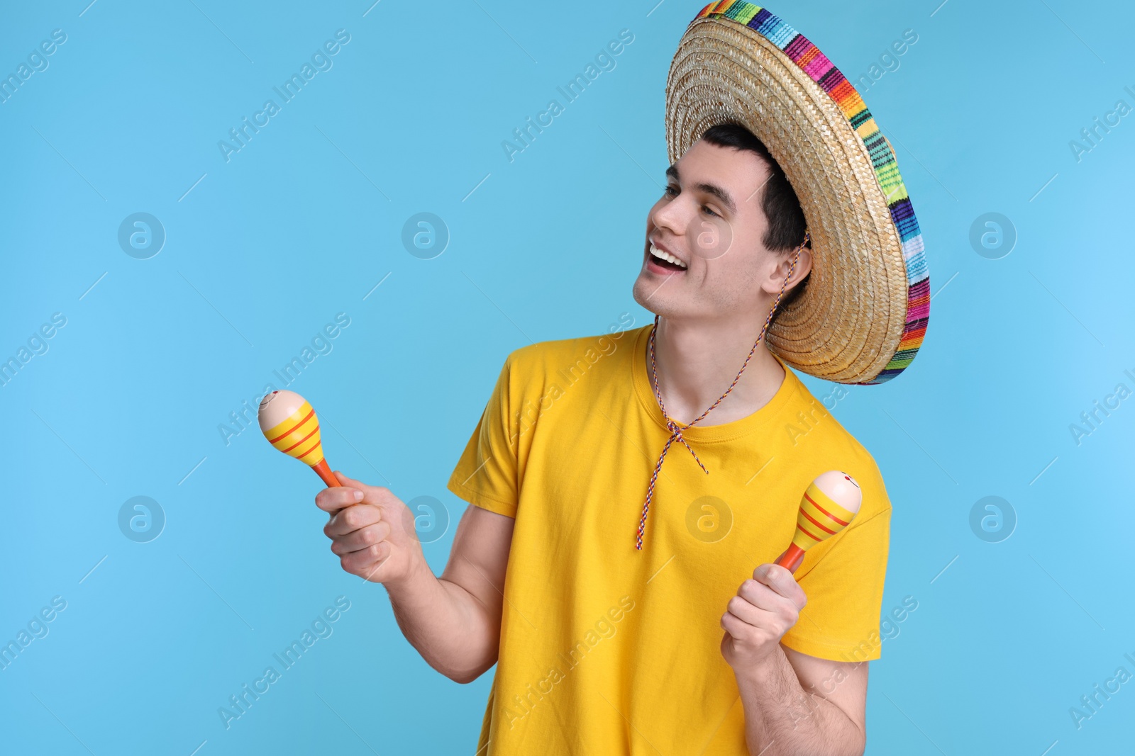 Photo of Young man in Mexican sombrero hat with maracas on light blue background