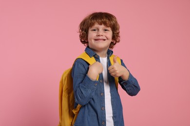 Happy schoolboy with backpack showing thumb up gesture on pink background