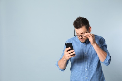 Man with vision problems using smartphone on grey background, space for text