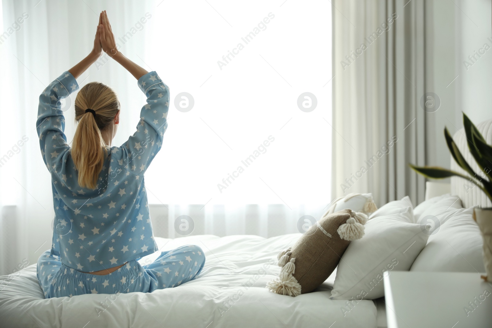 Photo of Young woman doing gymnastics on bed at home, back view. Morning fitness