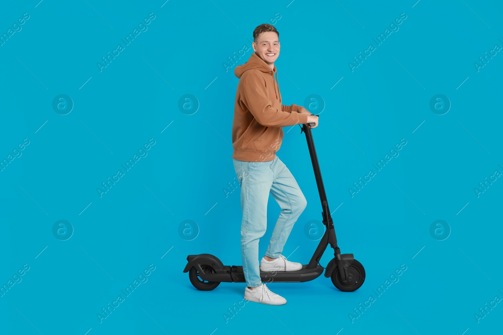 Photo of Happy man with modern electric kick scooter on light blue background