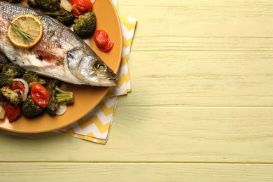 Photo of Delicious baked fish and vegetables on yellow wooden table, top view. Space for text