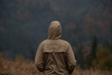 Photo of Woman in raincoat enjoying mountain landscape under rain, back view