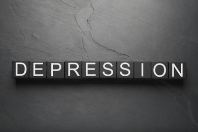 Photo of Word Depression made of black wooden cubes on dark table, flat lay