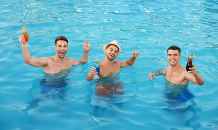 Happy young friends with refreshing cocktails in swimming pool