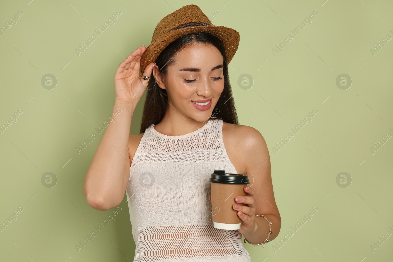 Photo of Beautiful young woman with straw hat and cup of coffee on olive background. Stylish headdress