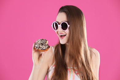 Photo of Beautiful young woman wearing sunglasses with donut on pink background