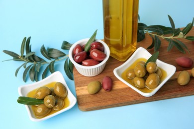 Photo of Bottle of oil, olives and tree twigs on light blue background