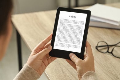 Image of Woman using e-book reader at wooden table indoors, closeup