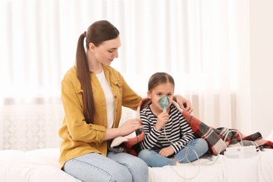 Photo of Mother helping her sick daughter with nebulizer inhalation in bedroom