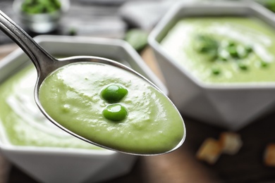 Spoon with fresh vegetable detox soup made of green peas on blurred background, closeup