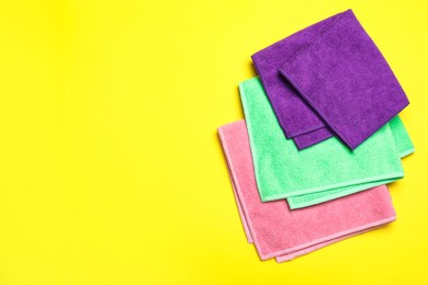 Photo of Colorful microfiber cloths on yellow background, flat lay. Space for text