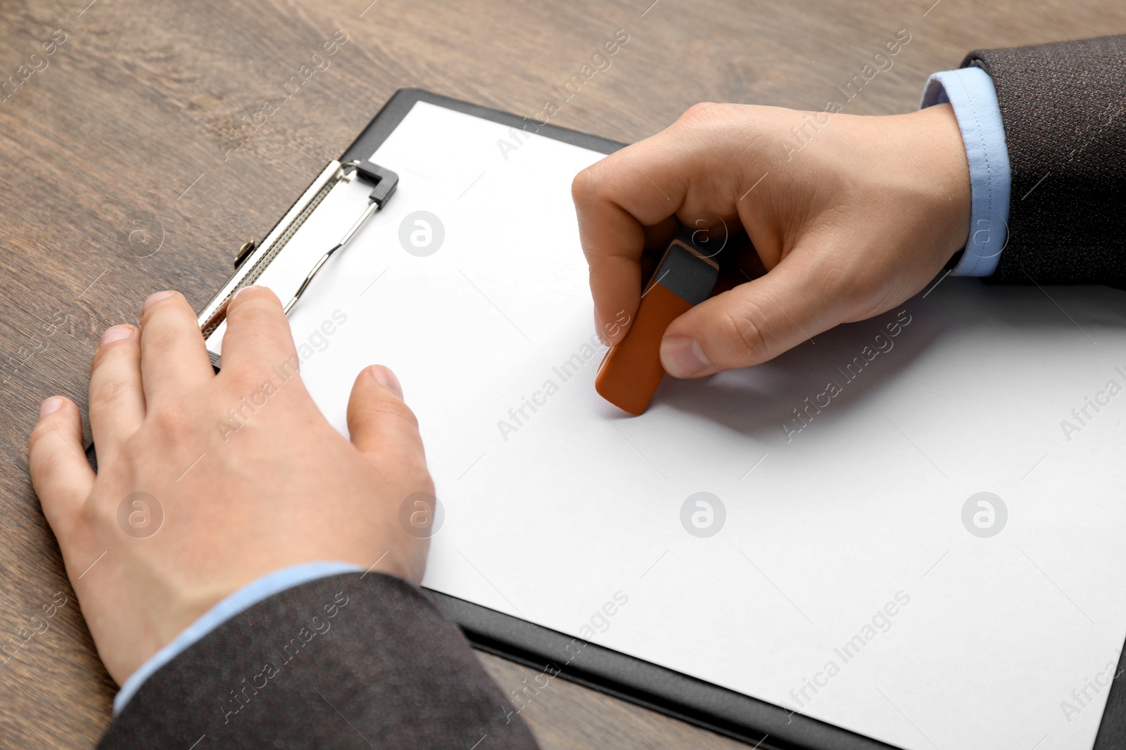 Photo of Man erasing something on paper at wooden table, closeup