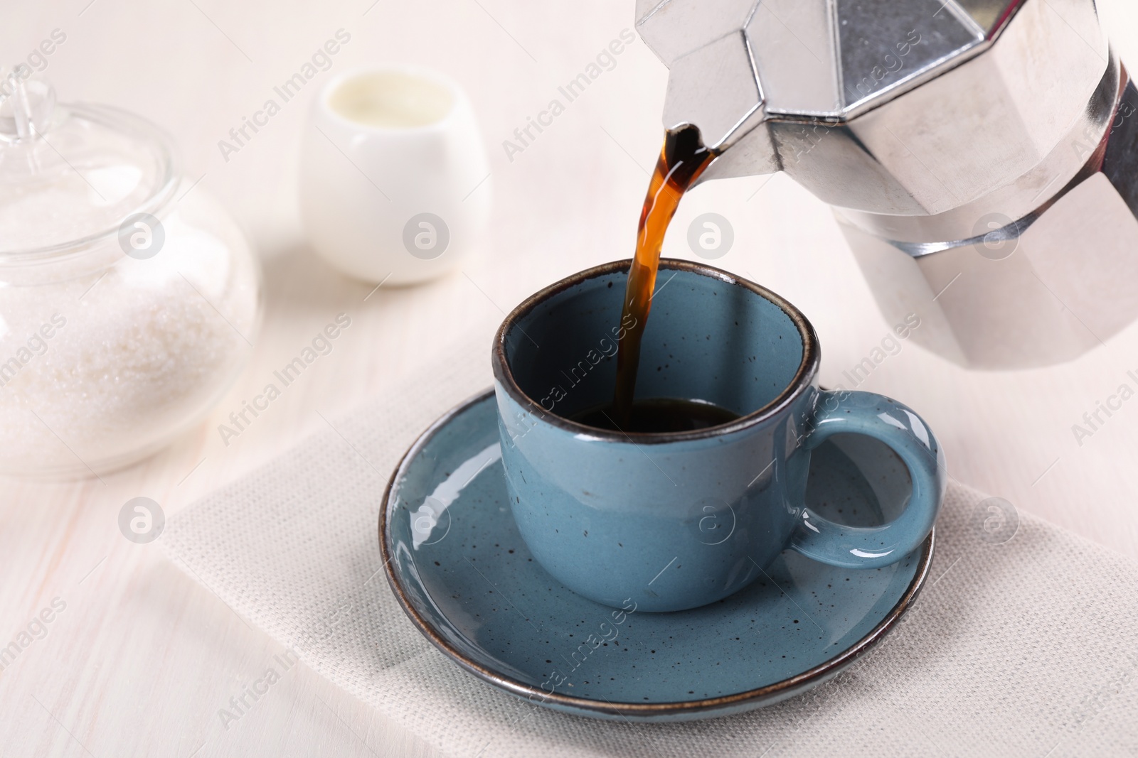 Photo of Pouring aromatic coffee from moka pot into cup at white wooden table, closeup