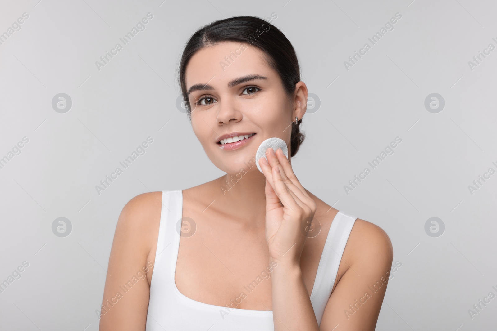 Photo of Young woman cleaning her face with cotton pad on light grey background