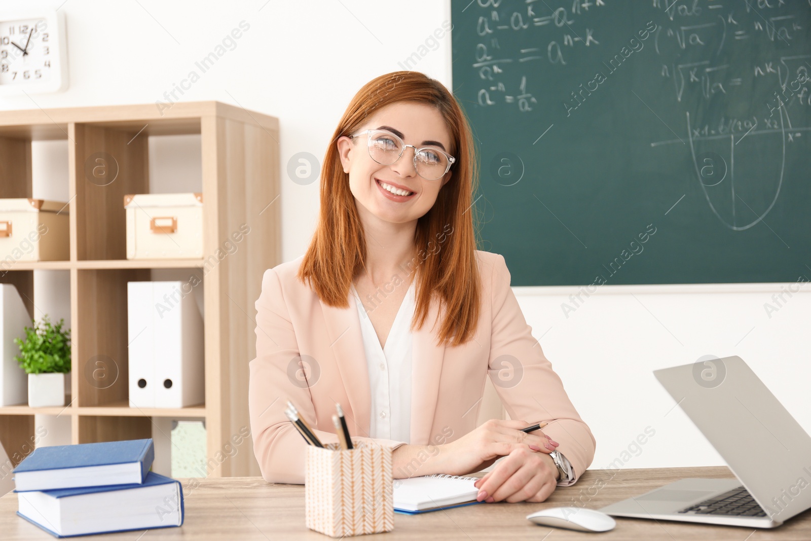 Photo of Beautiful young teacher working at table in classroom