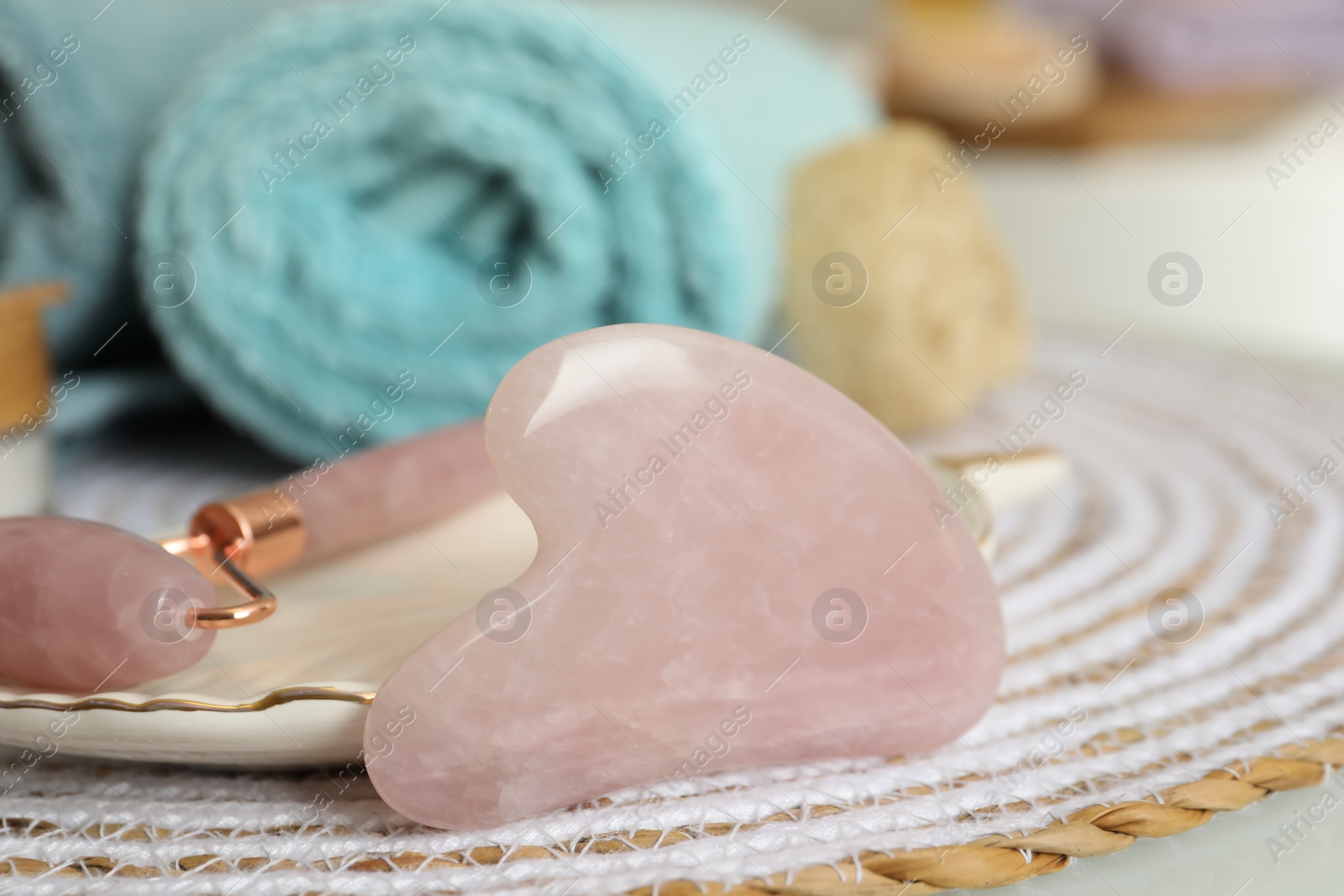 Photo of Rose quartz gua sha tool, natural face roller and towel on table in bathroom, closeup