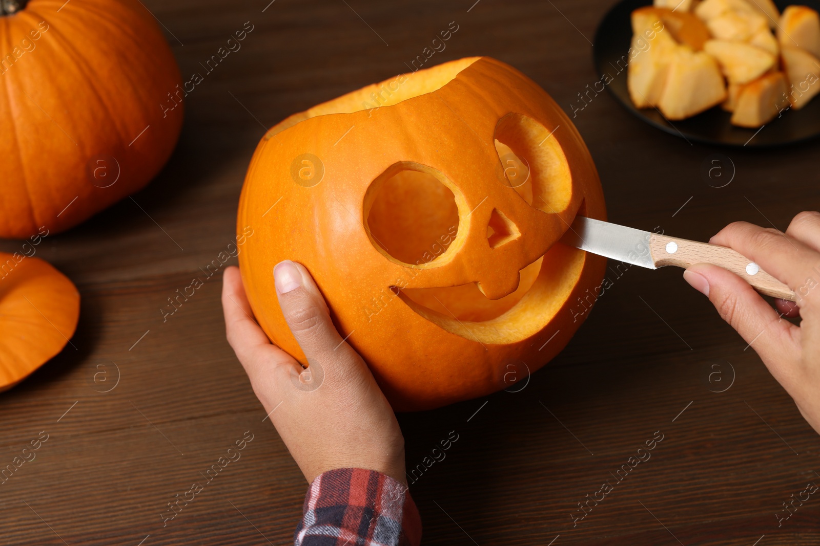 Photo of Woman carving pumpkin for Halloween at wooden table, closeup