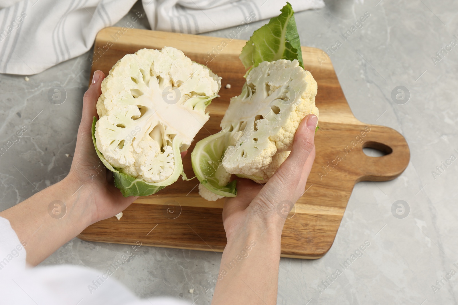 Photo of Woman with halves of fresh cauliflower at light grey table, closeup