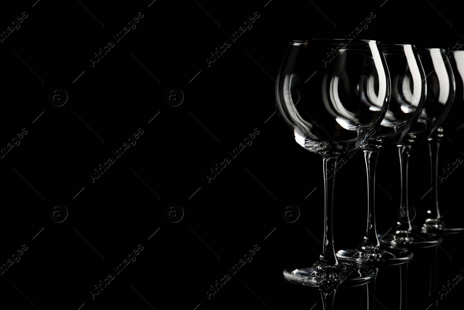 Photo of Set of empty wine glasses on black background. Space for text