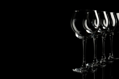 Photo of Set of empty wine glasses on black background. Space for text