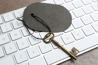 Vintage key with blank tag and keyboard on grey table, closeup. Keyword concept