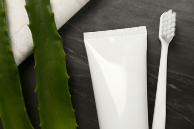 Aloe vera toothpaste in blank tube, brush and green leaves on black marble board, top view. Space for text