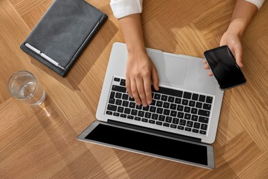 Photo of Woman with modern smartphone and laptop at wooden table, top view. Searching information